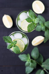 Obraz premium Two glasses of homemade citrus lemonade mojito with slices of lime, mint and ice on a dark wooden background.Top view.