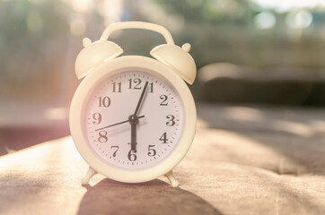 white alarm clock stands on the sofa in the sunlight. Beautiful background with alarm clock