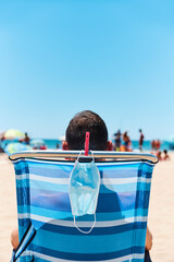 mask and man sitting in a deck chair on the beach