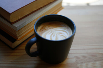 Wooden table background with cup of hot drink with milk art and stack of books, education during coffee break 
