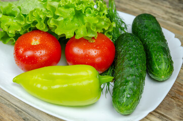 Fresh juicy vegetables peppers, tomatoes, cucumbers lettuce leaves with water drops beautifully laid out on a white plate close-up. Vegetables are in the form of a funny face