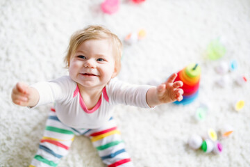 Fototapeta premium Adorable cute beautiful little baby girl playing with educational toys at home or nursery. Happy healthy child having fun with colorful wooden rainboy toy pyramid. Kid learning different skills.