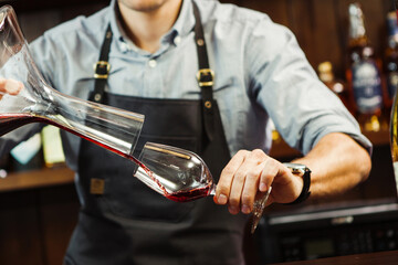 Sommelier pouring wine into glass from mixing bowl. Male waiter