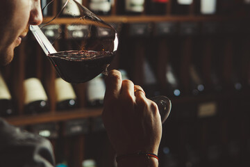 Close-up shot of young sommelier smell red wine on wine cellar background. - obrazy, fototapety, plakaty