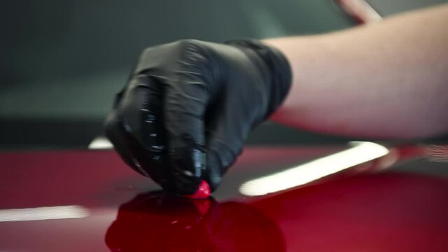 The master removes small dirt pieces from the car bonnet surface with special clay before polishing. Professional car washing and detailing process.