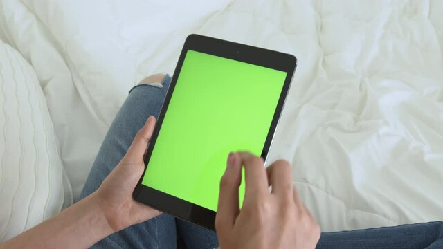 Woman holding digital tablet with green screen and touch device browsing Internet.