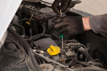 An auto mechanic works in black gloves opens the engine with a screwdriver. selective focus.