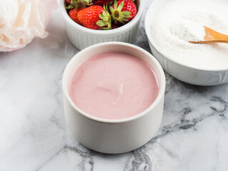 Collagen protein powder in bowl with wooden spoon on marble table. Adding collagen supplement to strawberry yogurt