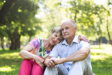 Happy Elderly Senior couple sitting on grass together relaxing in the garden.