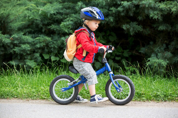 Naklejka premium Cute toddler boy with blue helmet, riding balance bike on the street