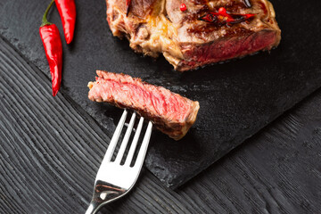 Sliced grilled meat barbecue steak Striploin with knife and fork carving set on black stone slate