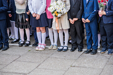 Little kids, schoolchildren stand in a row at the celebration of the beginning of the school year of tremest. Dressed in a school uniform, holding flower bouquets for teachers. The first time in first