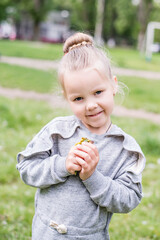 Little blond girl with blue eyes, hair arranged in a bun, wearing a gray dress, close-up portrait, looking into the camera, smiling, bored, playing on a lawn, sitting on the machine tires. Preschool  