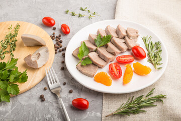Boiled pork tongue with tomatoes and herbs on a gray concrete background. Side view, close up.