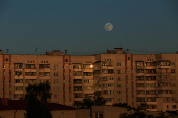 large white full moon on clear blue over an urban high building