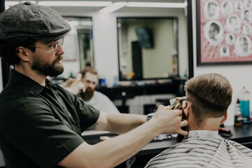 Handsome bearded man is getting haircut with razor by hairdresser at the barbershop