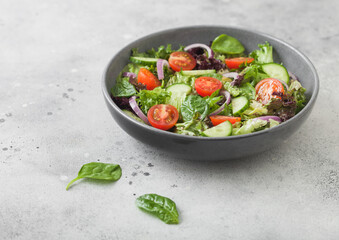 Healthy fresh vegetables salad with cucumbers and tomatoes, red onion and spinach in grey bowl on dark background