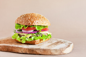Beef burger with fresh salad, cheese and tomatoes on wooden cutting board.