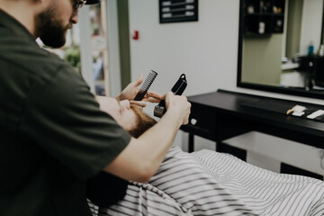 Getting perfect shape. Close-up side view of young bearded man getting beard haircut by hairdresser at barbershop