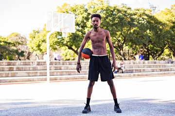 Young athletic black man playing on court with ball, basketball game player, morning exercises, active healthy lifestyle, hot summer day, streetball. 