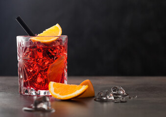 Negroni cocktail in crystal glass with orange slice and black straw on brown background.