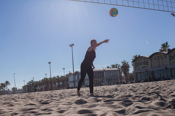Fototapeta na wymiar Beach volleyball, summer vacation, sport and people concept - young woman with ball playing volleyball on beach.