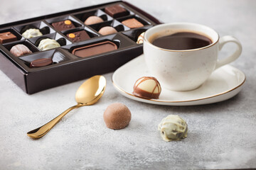 Box of Luxury Chocolate candies selection with cup of black coffee and golden spoon on light table background.