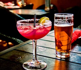 Refreshing drinks: colorful margarita with lime along with a foamy draught craft beer on a wooden table in a restaurant, ready to be enjoyed.