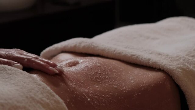 Cleansing massage for the body. Body scrub for clean skin. Masseur massages the stomach of a girl close-up.