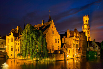 Fototapeta na wymiar Famous view of Bruges tourist landmark attraction - Rozenhoedkaai canal with Belfry and old houses along canal with tree in the night. Brugge, Belgium