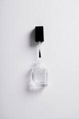 Vertical overhead shot of a clear open nail polish bottle with the applicator on a white background