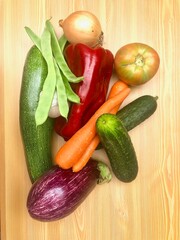 Verduras frescas de la huerta: pimiento, pepino, berenjena, zanahorias, ajo, judias verdes, tomate. Sobre fondo madera clara mesa.