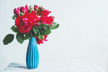 Bouquet of red roses in a blue vase on a white background, Place for text.