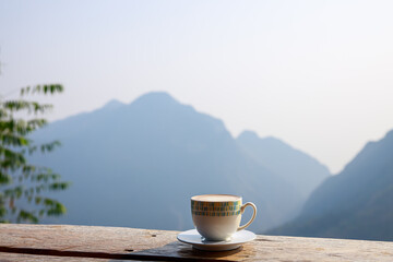 hot cup of coffee is placed on a wooden terrace and mountain background