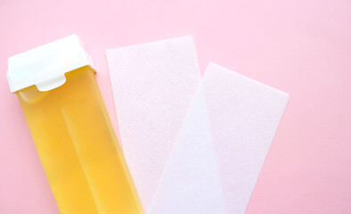 yellow wax cartridge, two paper strips for depilation and a razor on a pink background. Beauty,...