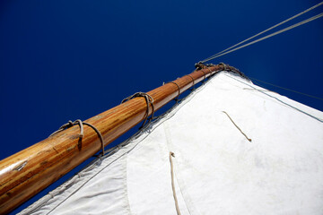 Wooden mast and white sail on the blue sky background