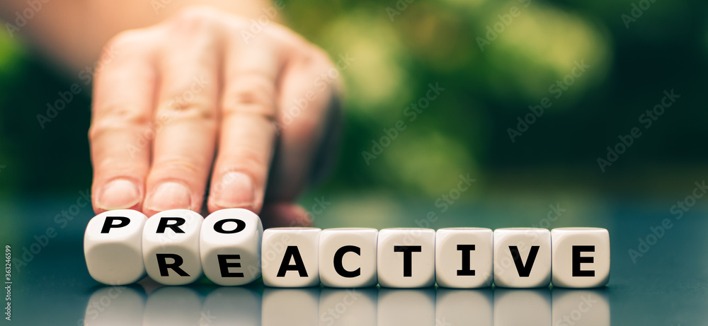 Wall mural hand turns dice and changes the word reactive to proactive.