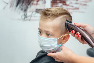 Child boy sitting in protective mask at the hairdresser cutting a haircut.