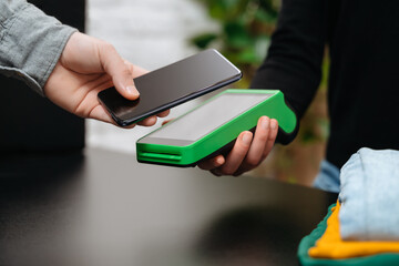 Close-up of customer person making payment via nfc terminal and mobile phone in clothes shop. Pay with smartphone. Contactless nfc and modern device technology concept
