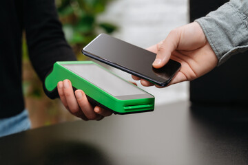 Closeup of man's hand with smartphone near nfc terminal on counter in store. Customer using smartphone for contactless payment via nfc terminal. Contactless payment and NFC technology concept
