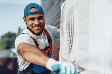 Young black man repairman checking an outside air conditioner unit