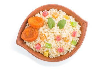 Bulgur porridge with dried apricots and candied fruits in clay bowl isolated on white background. Top view, close up.