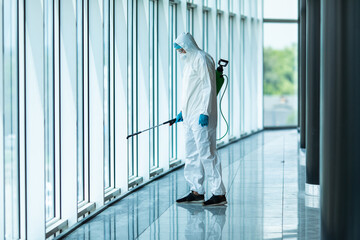 Coronavirus Pandemic. A disinfector in a protective suit and mask sprays disinfectants in office....