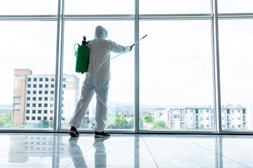 Coronavirus Pandemic. A disinfector in a protective suit and mask sprays disinfectants inoffice....