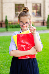 Back to school. Education concept. Cute smiling schoolgirl in glasses pointing up by forefinger near the school