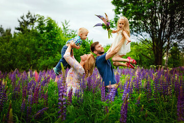 Family mom, dad, son and daughter in a blooming field with purple Lupin in a blooming field. Parents hold children in their arms. Lupin flowers are blooming.