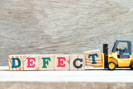 Toy forklift hold letter block T to complete word defect on wood background