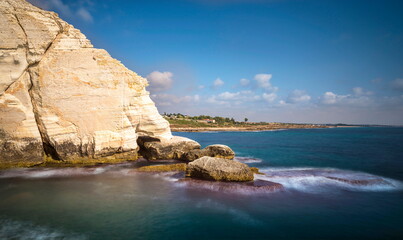 Beautiful Israeli landscape with white chalk cliffs of Rosh HaNikra grottoes, on the northern border of Israel, with the Mediterranean Sea coast and Nahariyya city in the background; Western Galillee