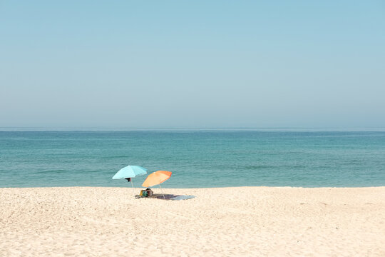 Daylight photo of two sunshades on a white sand beach with the sea as background.