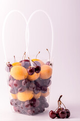 Cherry and apricot fruits in a transparent plastic box on a white background.